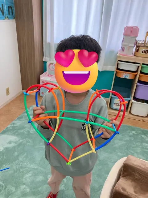 カラフルなパーツで作ったハート型の工作を持つ子ども