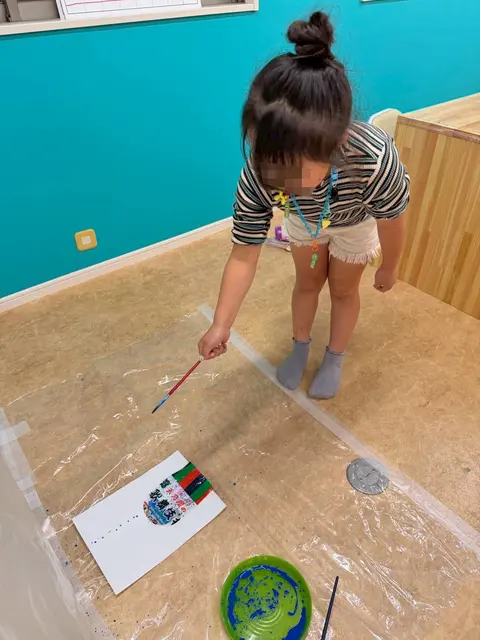 床に広げた紙に絵筆で絵を描く子ども