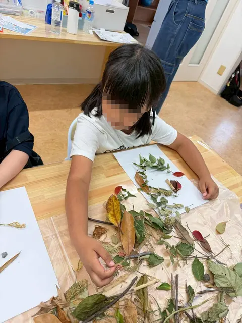 葉や枝を使って顔のような自然アートを作る子ども