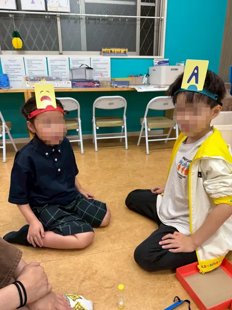 アルファベットのカードを頭に付けて遊ぶ子どもたち