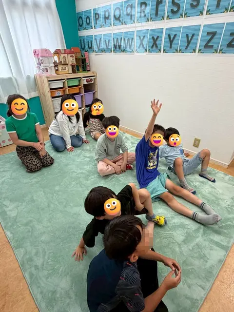 教室の床に座って手を挙げる子どもたち
