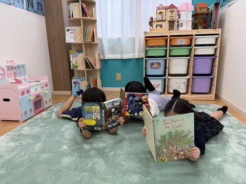プレイマットに寝転んで英語の絵本を読む子どもたち