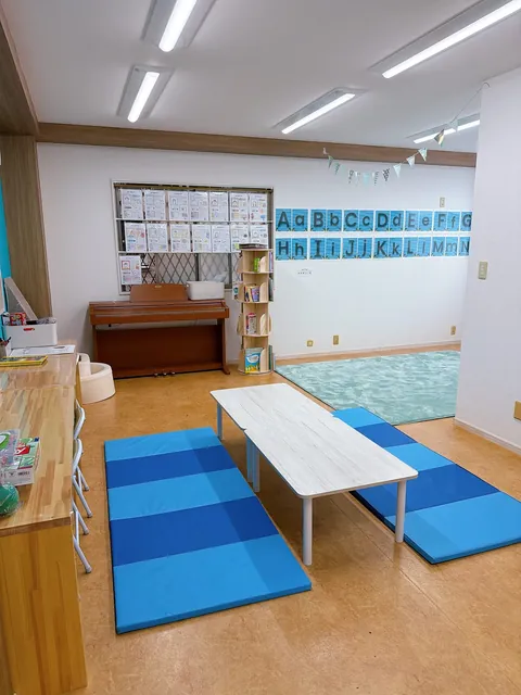 青いマットとピアノ、アルファベットの掲示がある教室