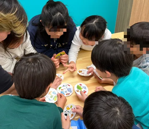 円形のカードを囲んで英語のカードゲームを楽しむアフタースクールの子どもたち