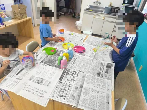 新聞紙を敷いて絵の具で工作をするアフタースクールの子どもたち
