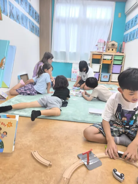 教室の床で電車のおもちゃやカードを広げて遊ぶアフタースクールの子どもたち
