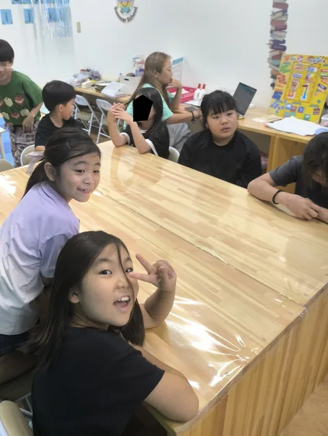 長いテーブルでピースサインをして笑顔を見せるアフタースクールの子どもたち