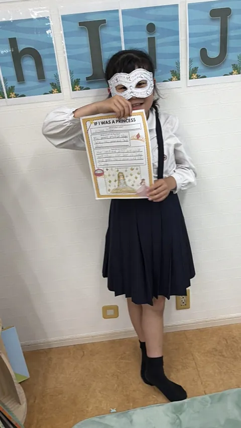 英語で書いた「If I Was a Princess」の作品を持つ仮面姿の女の子