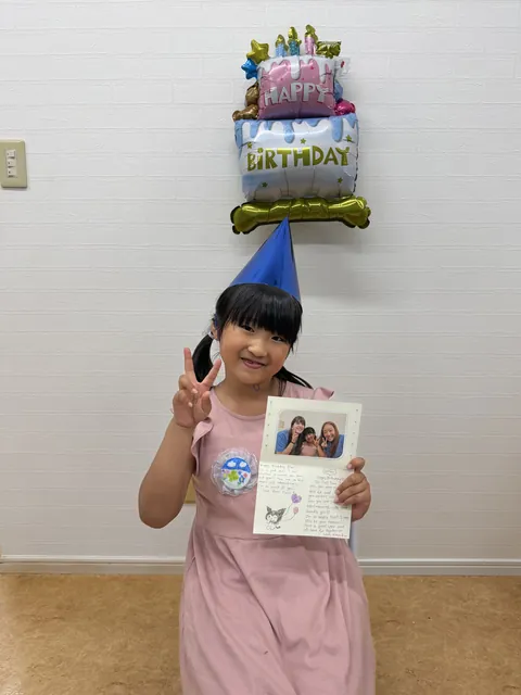 誕生日のバルーンの前でバースデーカードを持つ女の子