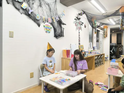 ハロウィン飾りの教室で、とんがり帽子をかぶってお誕生日をお祝いしてもらう女の子と先生