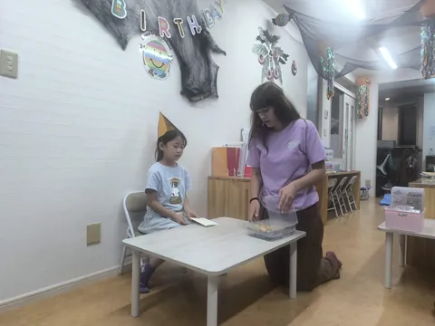 アフタースクールのお誕生日会で、先生からカードを受け取るとんがり帽子の女の子