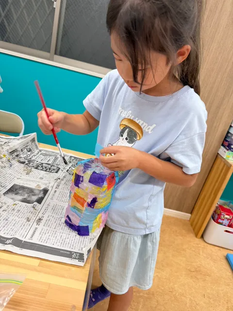ペットボトルにカラフルな紙を貼ってランタンを作る女の子