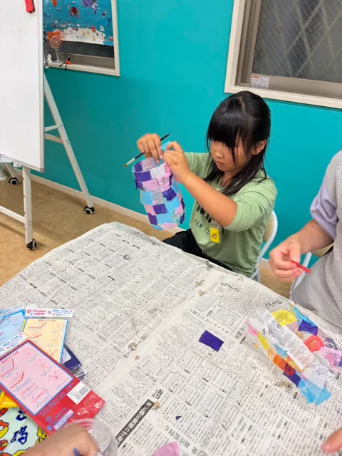 紫と水色の紙を貼ったランタンを手に持って確かめる女の子