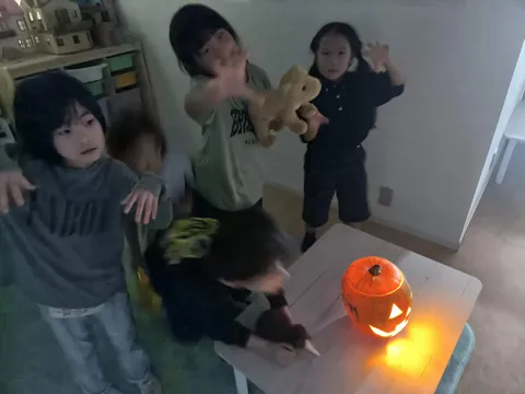 アフタースクールのハロウィンで、ジャック・オー・ランタンの明かりの前でおばけのポーズをする子どもたち