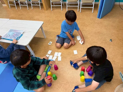 床に座ってカードやカップのゲームを楽しむアフタースクールの子どもたち