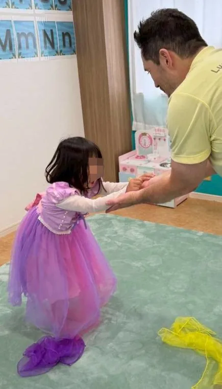 ドレスを着て先生と手をつなぐアフタースクールの子ども