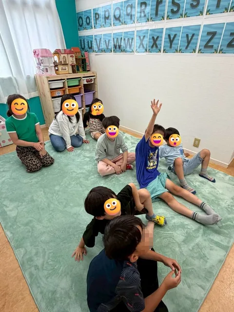 教室の床に座って手を挙げるアフタースクールの子どもたち