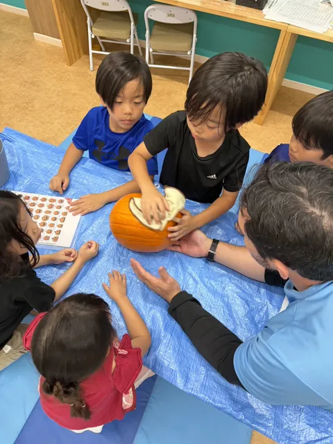 アフタースクールのハロウィンで、先生と一緒にかぼちゃを拭いてジャック・オー・ランタン作りの準備をする子どもたち