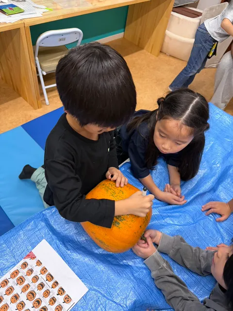 友だちに見守られながら、ペンでかぼちゃに顔を描く男の子