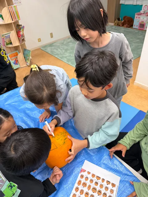 友だちと交代しながらかぼちゃに顔の線を描くアフタースクールの子どもたち