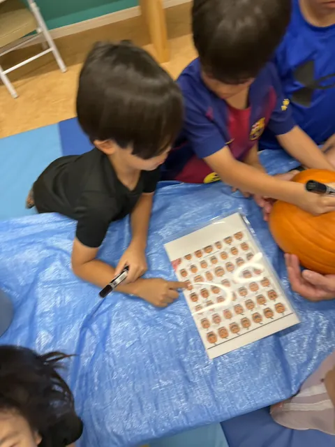ジャック・オー・ランタンの顔の見本シートを指さして、どの顔にするか選ぶ子どもたち