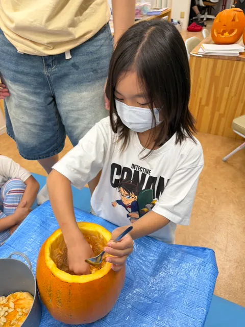 手とスプーンを使ってかぼちゃの種を取り出す女の子