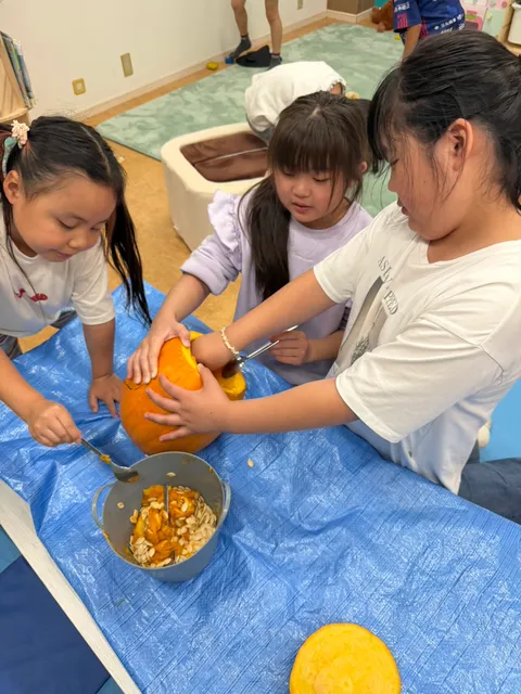 三人で協力してかぼちゃを傾け、スプーンで中身をかき出す女の子たち
