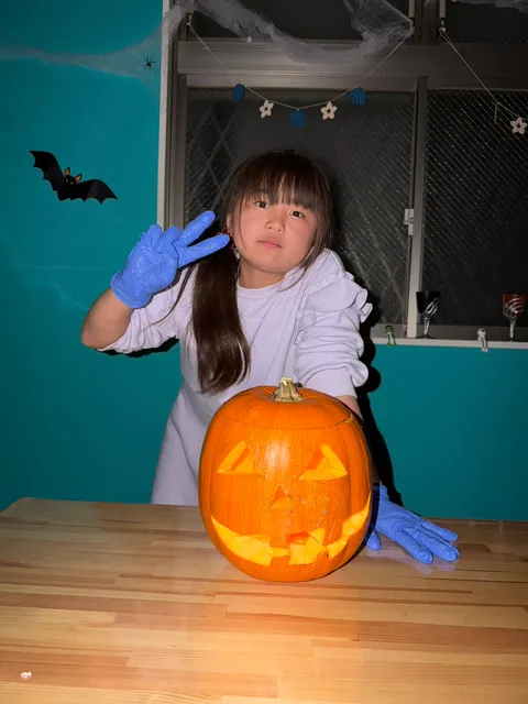 手袋をして、完成したジャック・オー・ランタンの横でピースをする女の子