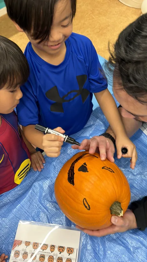 かぼちゃに顔を描きながら笑顔を見せるアフタースクールの男の子と先生