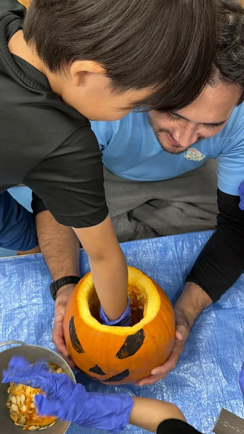手袋をしてかぼちゃの中の種をかき出す子どもと、そばで見守る先生