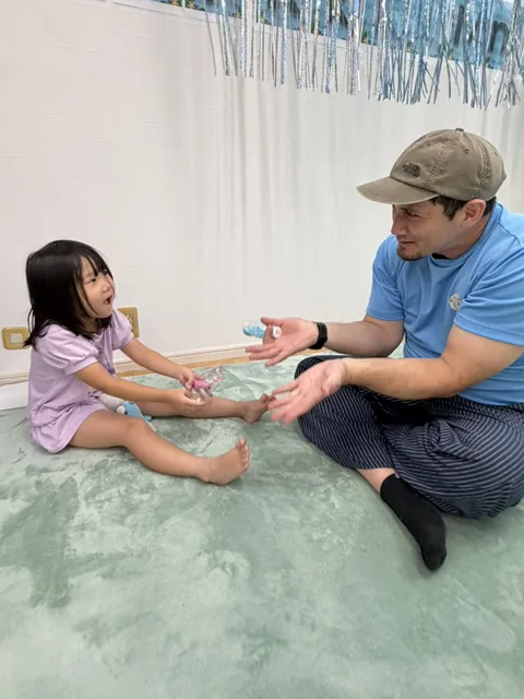 キンダースクールで先生と手を伸ばしてやりとりを楽しむ子ども