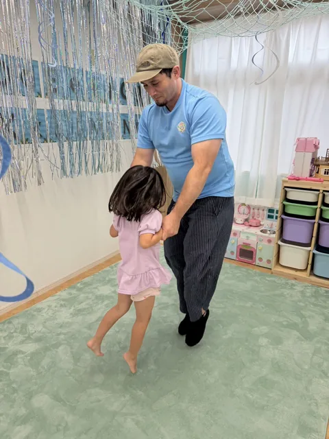 キンダースクールで先生と手をつないで踊る子ども