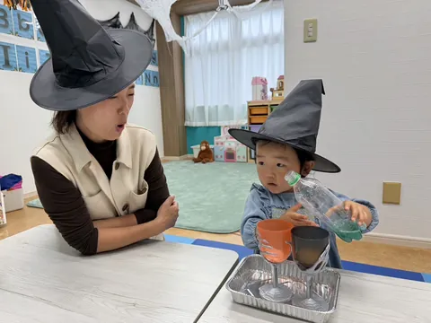 魔女の帽子をかぶったお母さんの横でペットボトルの色水を注ぐ女の子