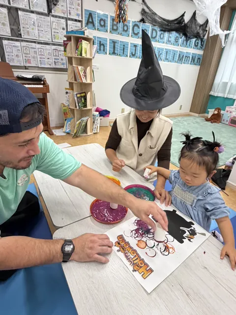 先生とお母さんと一緒にハロウィンのスタンプアートを作る女の子