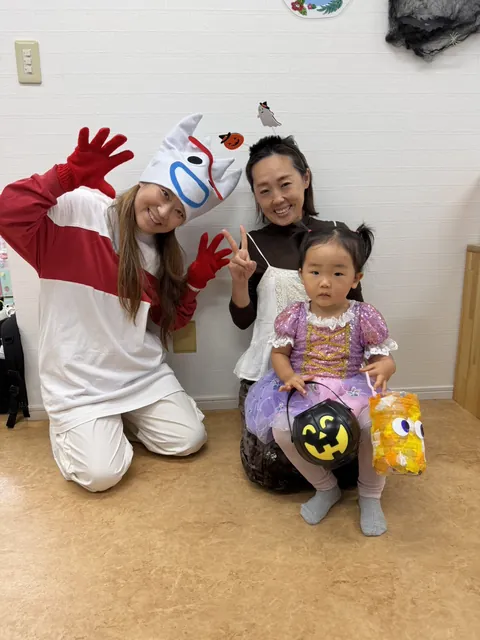 フォーキーの仮装をした先生とお母さんと一緒に、手作りのおばけとバケツを持って記念撮影する女の子