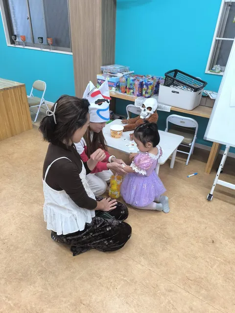 ハロウィンの帽子をかぶった先生にタトゥーシールを貼ってもらう、紫のドレスの女の子