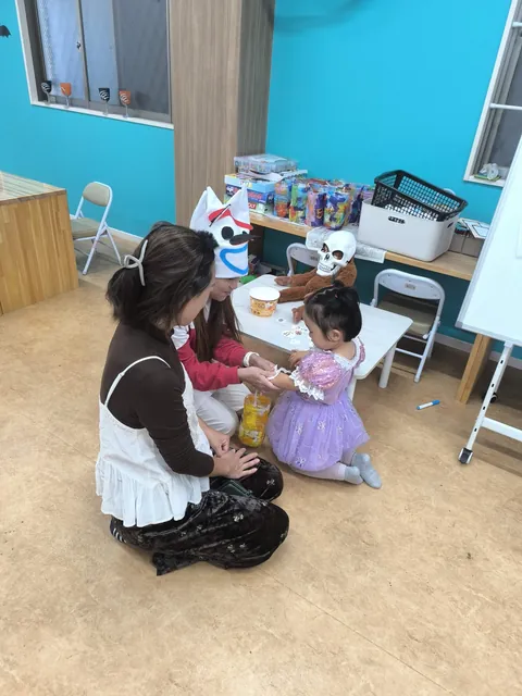 ピーカブーのハロウィンで、お母さんのとなりで先生にシールを貼ってもらう女の子