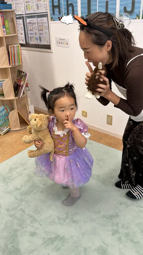 お母さんの「しーっ」をまねして、ぬいぐるみを抱っこしながら人差し指を口に当てる女の子