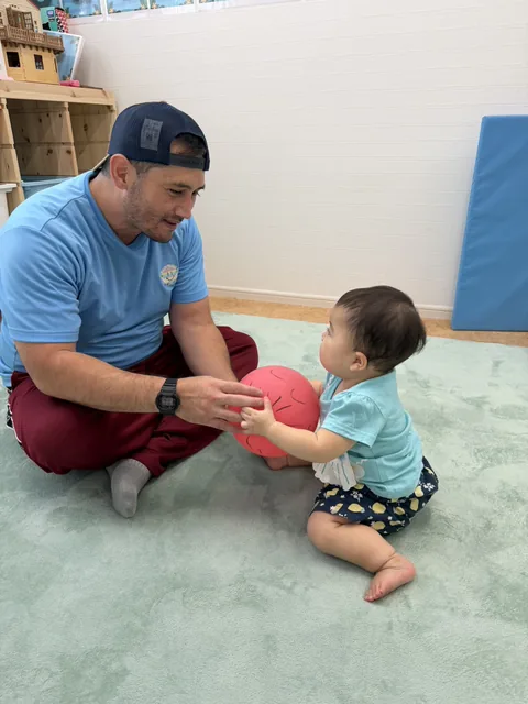 プリスクールで先生とボールのやりとりを楽しむ赤ちゃん
