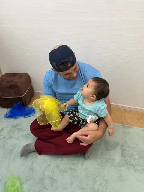 プリスクールで先生に抱っこされてスカーフ遊びをする赤ちゃん