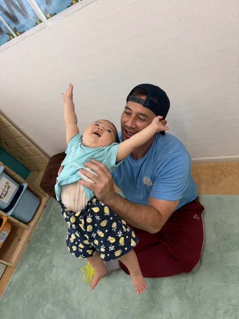 プリスクールで先生に抱き上げられて笑顔を見せる赤ちゃん