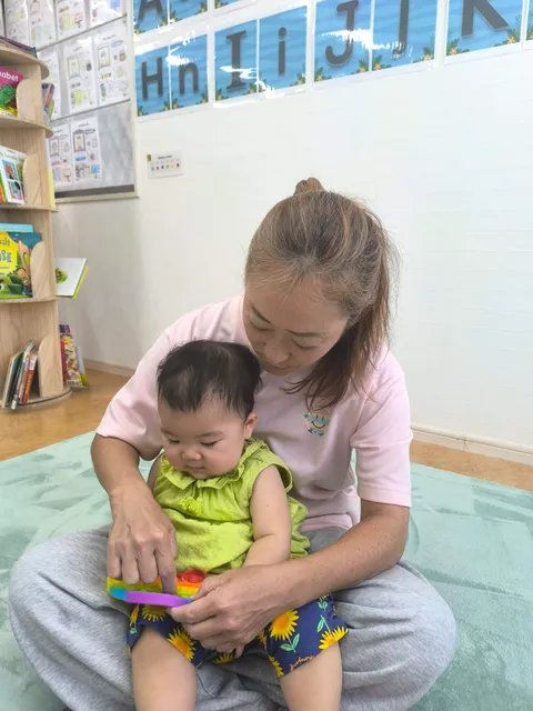 プリスクールで先生に抱っこされておもちゃで遊ぶ赤ちゃん