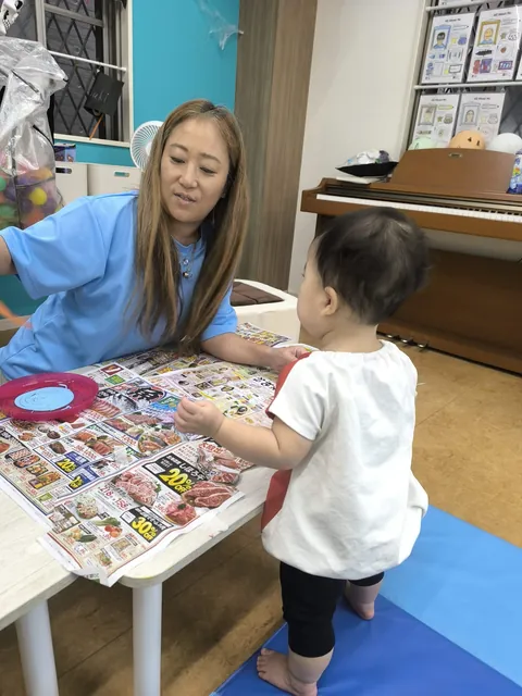 プリスクールでテーブルの前に立ち先生とやりとりする赤ちゃん