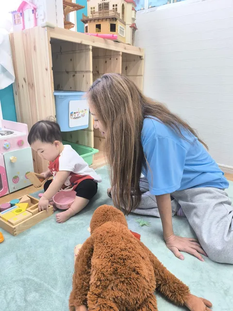 プリスクールで先生に見守られながら木のブロックで遊ぶ赤ちゃん