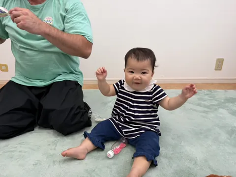 プリスクールで先生のとなりで両手を上げてにっこり笑う赤ちゃん