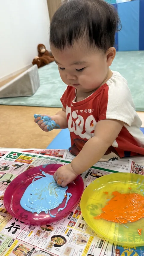 プリスクールで青とオレンジの絵の具を手でさわってみる赤ちゃん