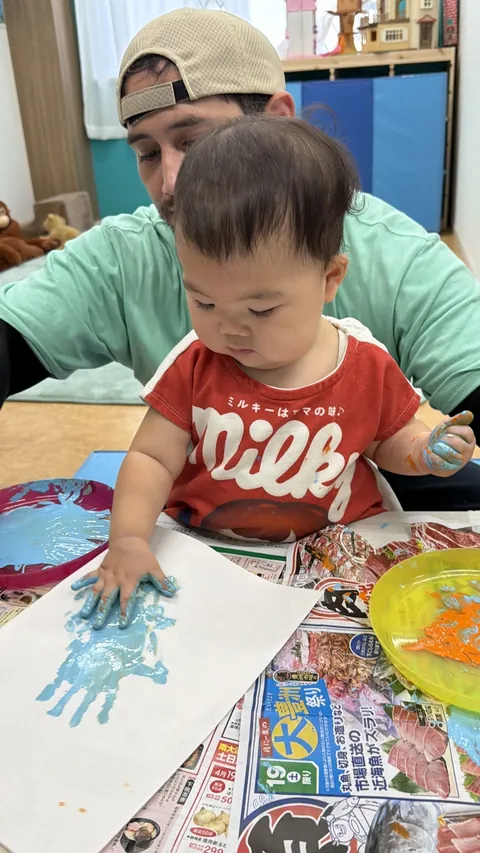 プリスクールで先生と一緒に青い絵の具で手形アートを作る赤ちゃん