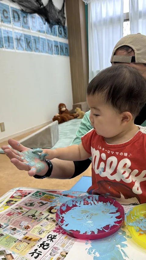 プリスクールで青い絵の具がついた手のひらを先生と見比べる赤ちゃん