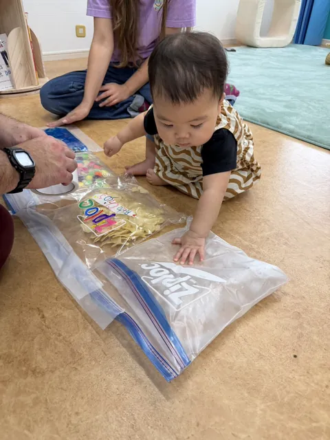プリスクールで先生と一緒に感触袋をさわって遊ぶ赤ちゃん