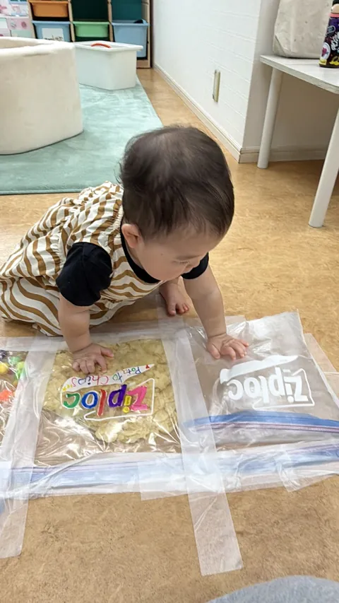 プリスクールで床に貼った感触袋の上をはいはいする赤ちゃん